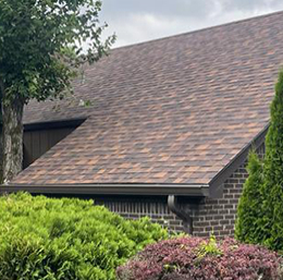 exterior residential roof with gutters on a brick house surrounded by shrubs