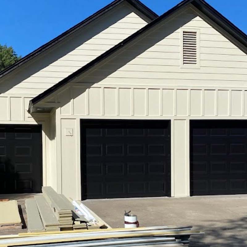 White Siding installation with black garage doors and a black roof