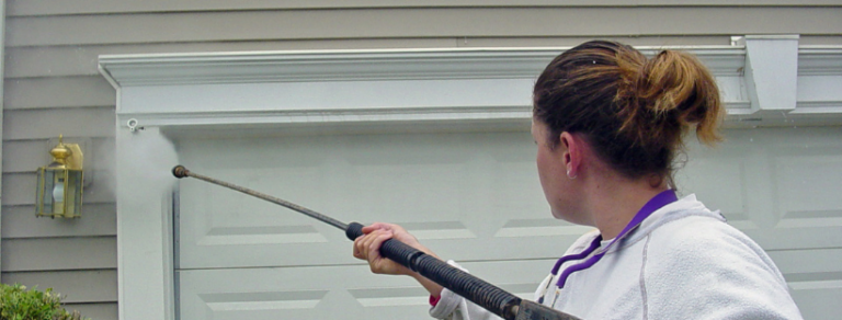 Woman in white Power Washing Vinyl Siding near a garage door