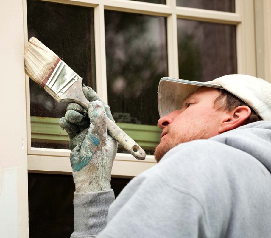 Exterior painting contractor with a brush painting near a window