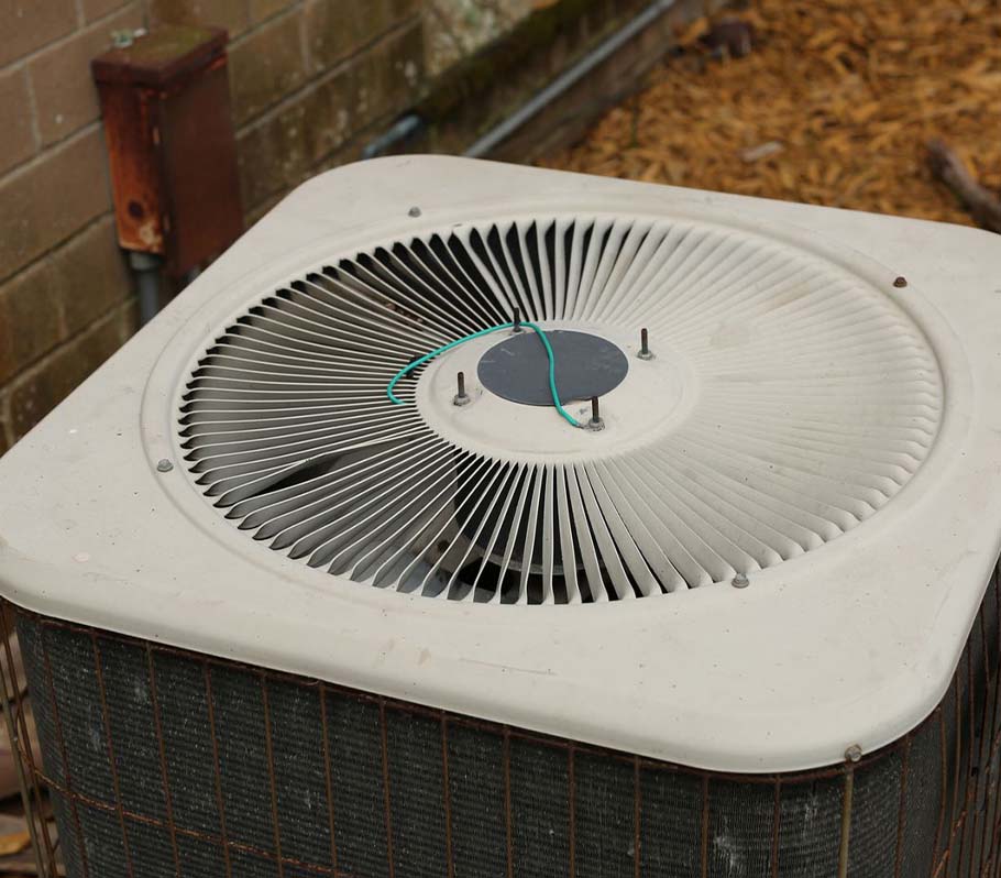 HVAC unit with green ground wire attached to top of fan next to a brick building
