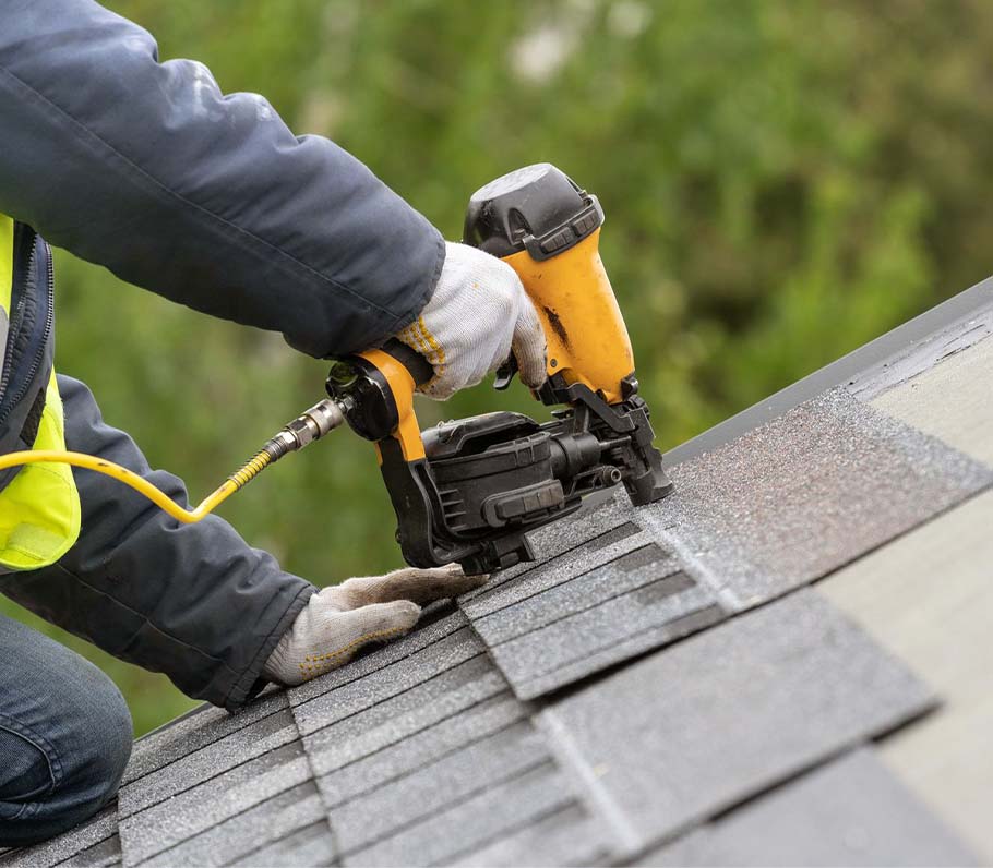 close up of a roofing contractor installing shingles with a yellow pnuematic nail gun