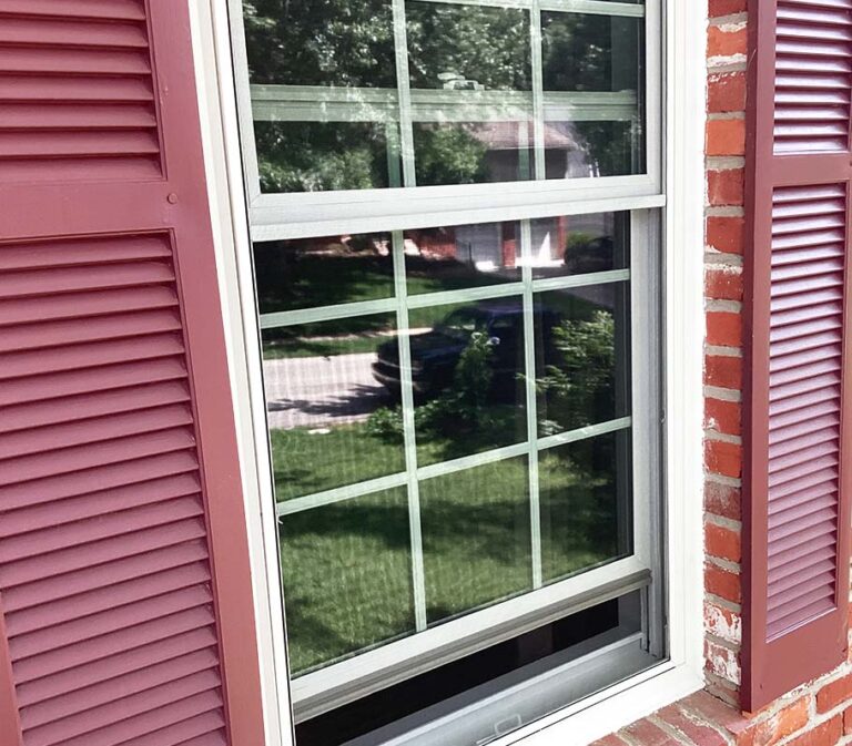 Pella White window surrounded by red shutters