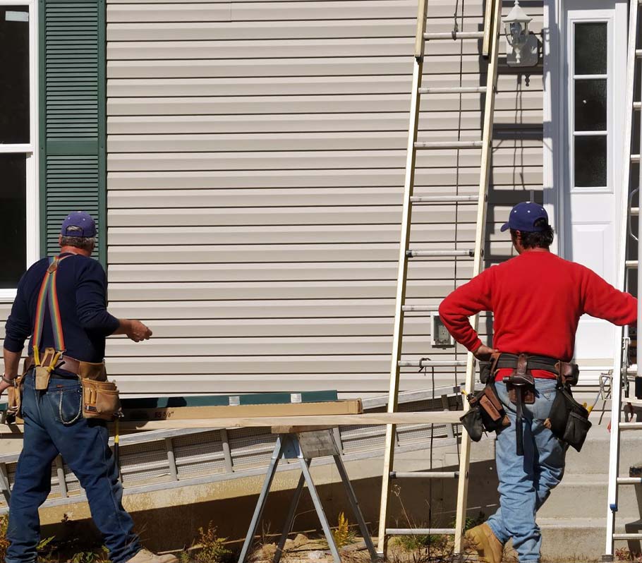 siding installers trimming exterior cladding in front of a residential home with ladders in the background