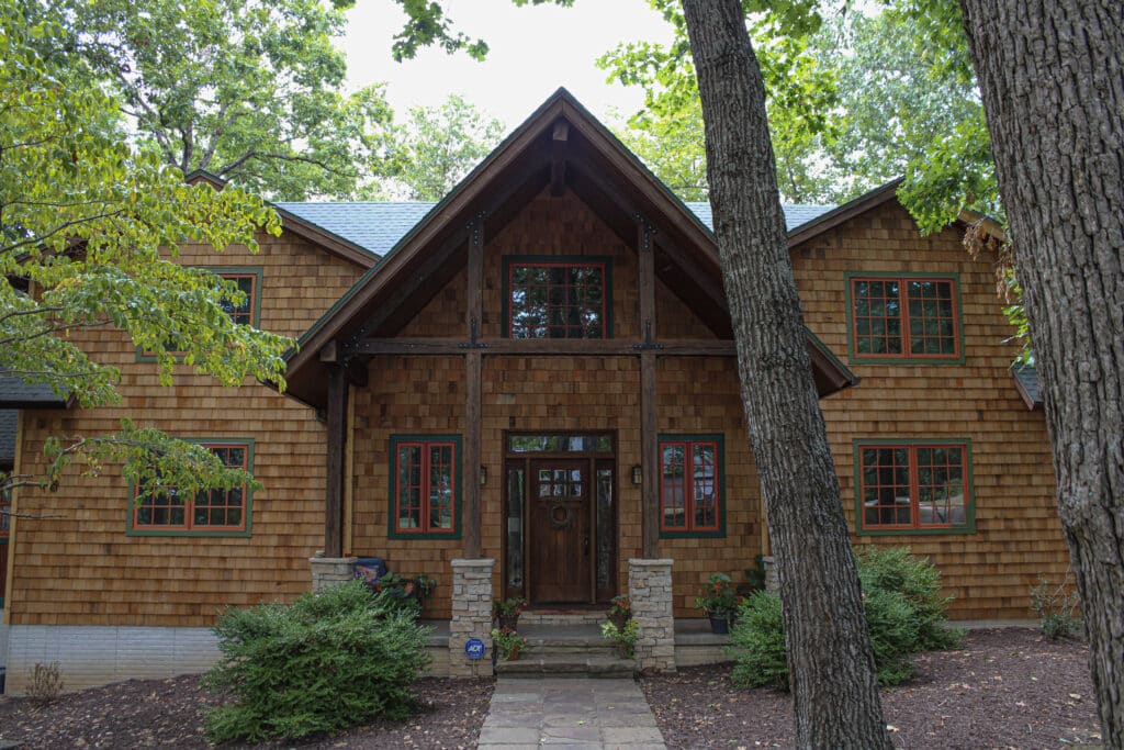 Cedar shake sided house with green roof and red windows installed by Xtreme Exteriors siding contractors.