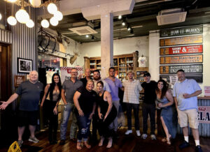 Group of people standing inside a bar with a "How It Works" sign in the background.