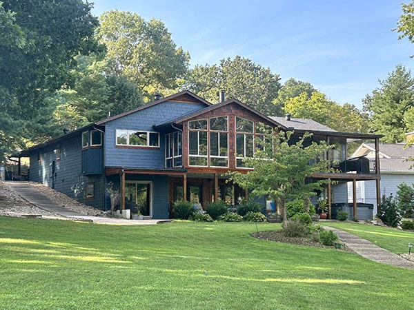 A two-story house with a mix of blue siding and large windows, surrounded by trees and a manicured lawn Xtreme Exteriors in Rogers, AR.