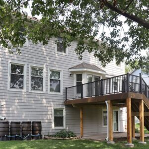 Two-story gray house with a balcony, surrounded by greenery.