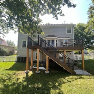 Backyard with a two-tiered wooden deck attached to a house, featuring black railings and stairs.