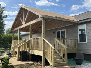 A newly constructed wooden porch, crafted by skilled deck builders in Nashville, features stairs and a roof extending from a gray house Xtreme Exteriors in Goodlettsville, TN.