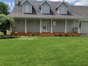 A two-story house with gray siding, expertly crafted by a renowned siding company in Springfield, features a white-trimmed front porch and multiple gables.