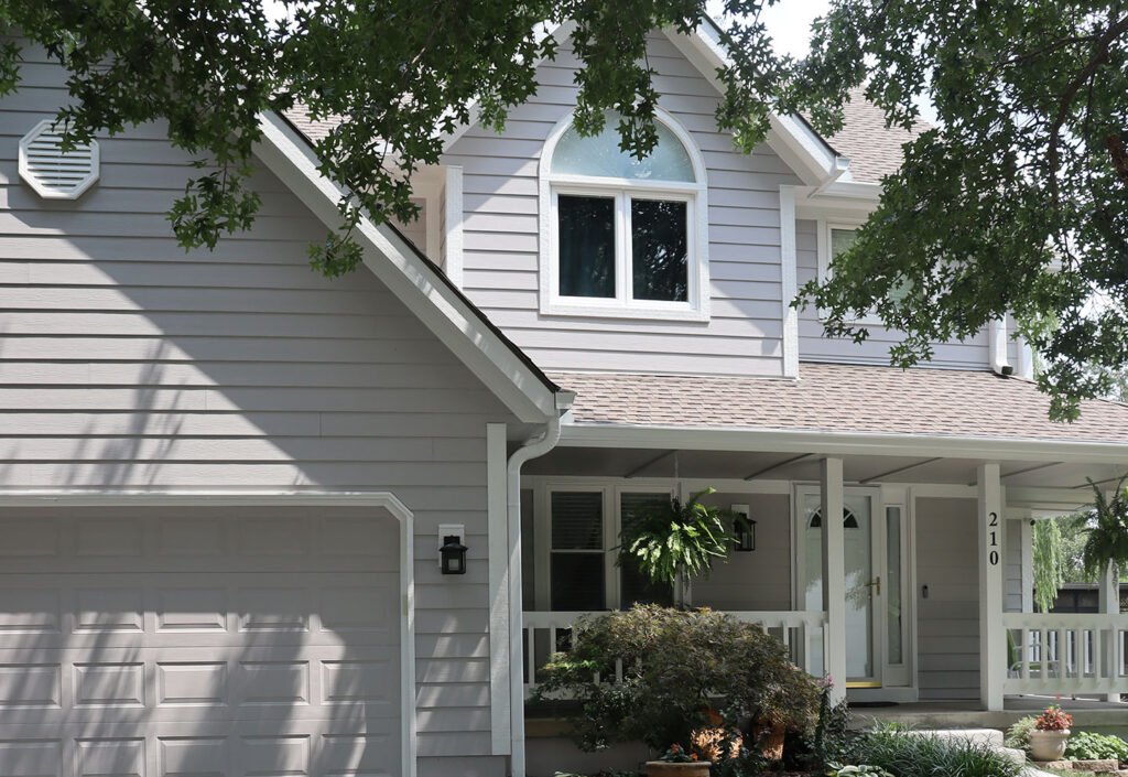 Two-story house with gray siding, white trim, and front porch with plants in Belton, MO | Xtreme Exteriors