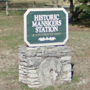 Green and white sign on a stone base reading "Historic Mansker's Station, a 1779 frontier fort," with a large circular stone embedded in the base