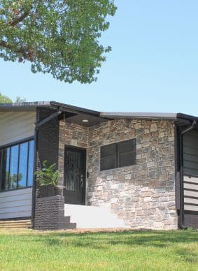 A mid-century modern house with a stone facade entryway featuring a black door with a decorative metal grate.