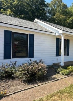 A white house with horizontal siding, dark gray shingle roof, and dark blue shutters.