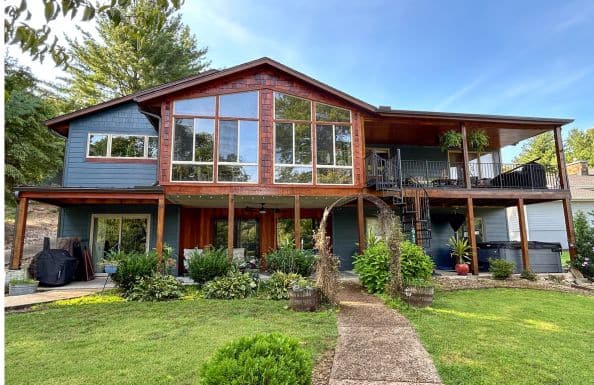 A two-story house with blue siding and wood accents, featuring a large wall of windows in the center.