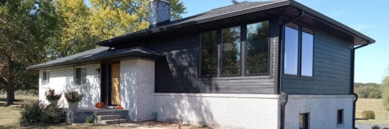 home with a white brick exterior, black siding, and a modern window addition.