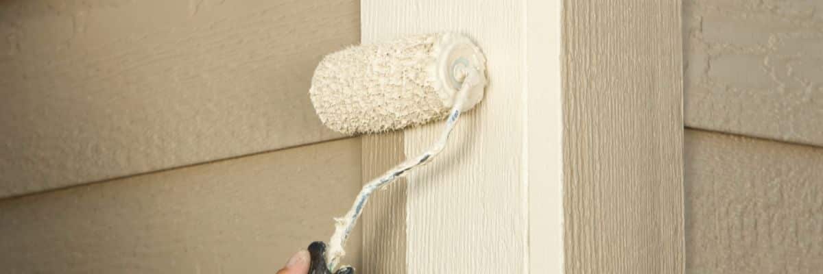 An exterior painters' paint roller with a thick nap applying beige paint to a textured wall