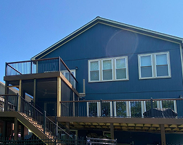 Two-story house with blue vinyl siding, multiple white-trimmed windows, and an elevated composite deck by Xtreme Exteriors