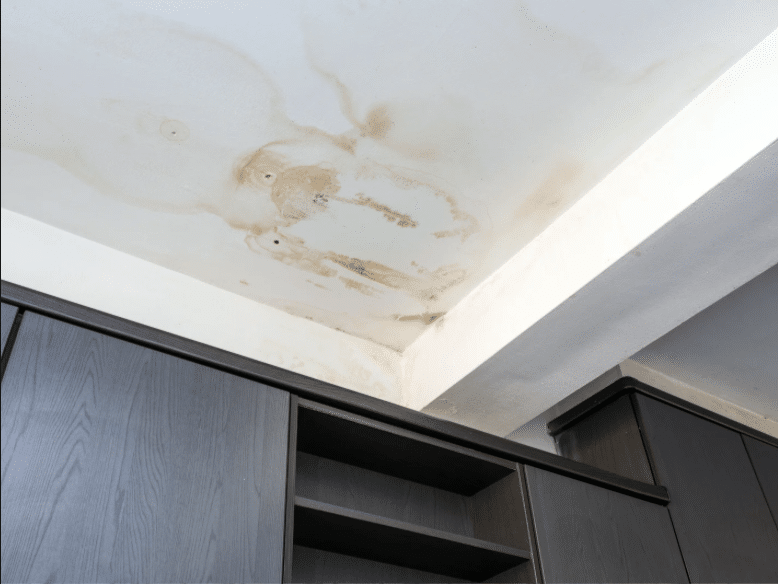 Visible water stain on a white ceiling above cabinets in a US home, caused by hail damage and indicating the need for ceiling inspection.