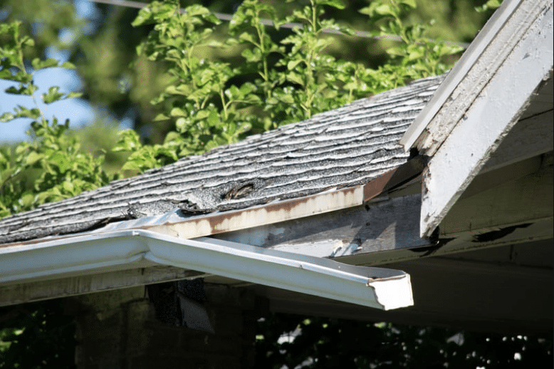 Damaged gutter on a residential roof in the US, showing a visible dent and bending caused by a hail storm.