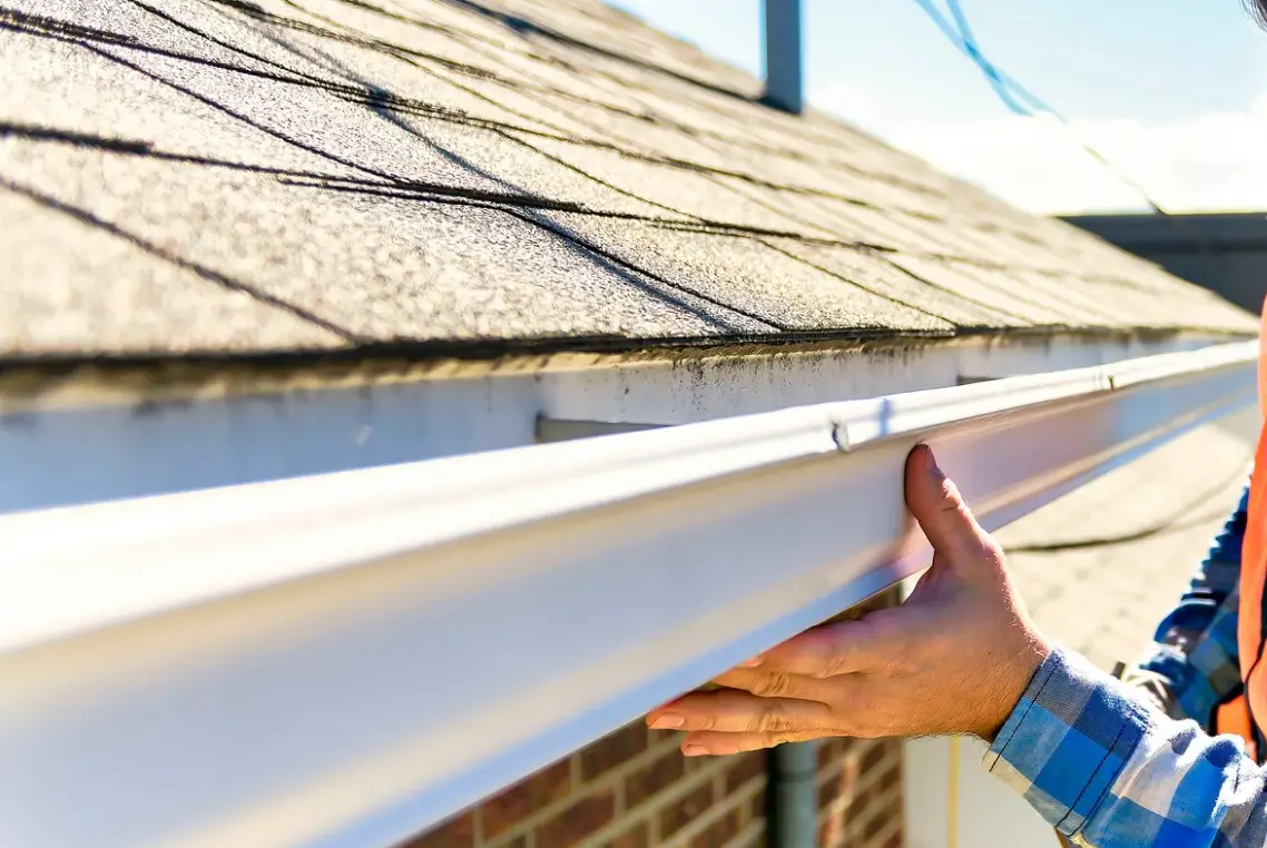 A technician examining the connection between roof shingles and the gutter on a residential home, emphasizing careful assessment and documentation for insurance roof damage claims by Xtreme Exteriors