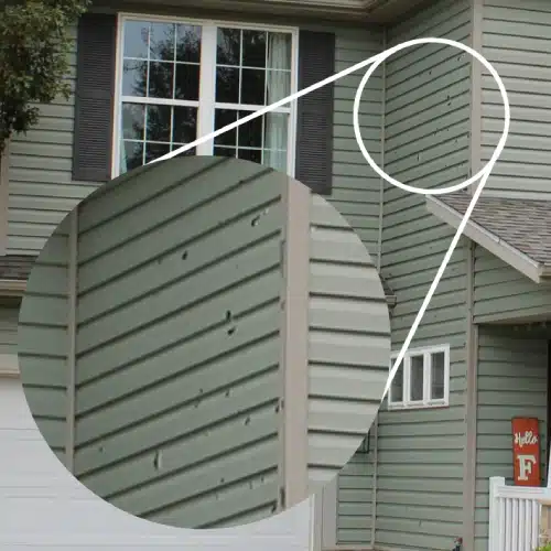 Zoomed-in view of hail damage on vinyl siding, a clear sign your Springdale home needs storm damage siding repair