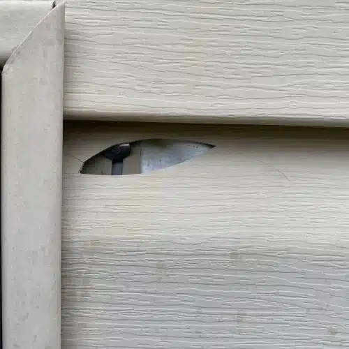 Close-up of beige vinyl siding with puncture damage requiring emergency siding repair Springdale