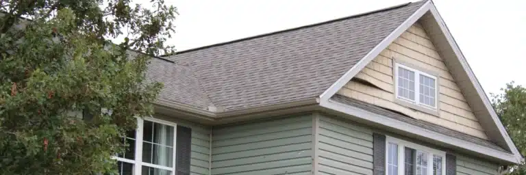 Warped and damaged beige vinyl siding on upper story of Springdale home, highlighting emergency siding repair Springdal
