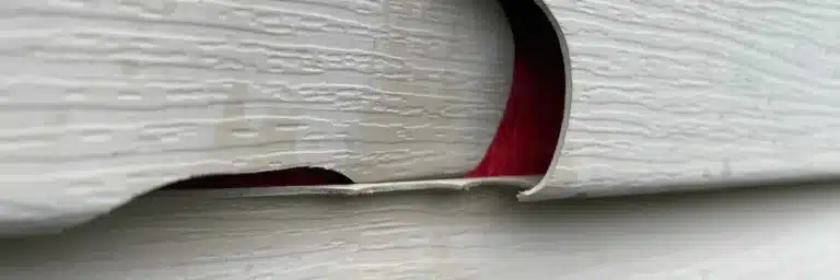 Close‑up of curled, cracked vinyl siding revealing red sheathing beneath, signaling urgent need for emergency siding repair Goodlettsville by Xtreme Exteriors in Goodlettsville, TN