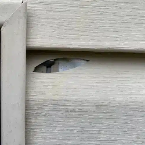 White vinyl siding with a significant horizontal hole exposing the underlayment, requiring emergency siding repair Shawnee by Xtreme Exteriors in Nixa, MO