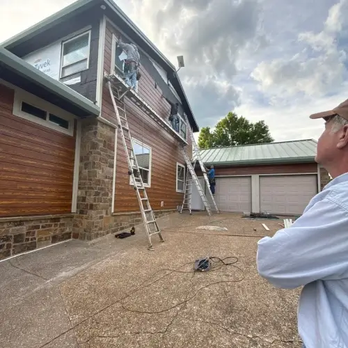 Technicians on ladders performing emergency siding repair on second story of Shawnee home with wood and stone exterio