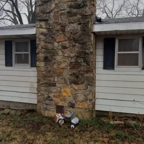 A stone chimney on a house with aged siding, indicating a need for siding maintenance by Xtreme Exteriors in Nixa, MO