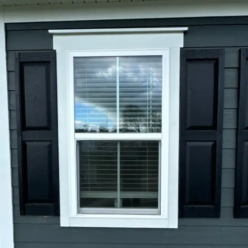 Choosing a siding contractor in Nixa, MO shown by expertly installed window trim, black shutters, and gray siding by Xtreme Exteriors