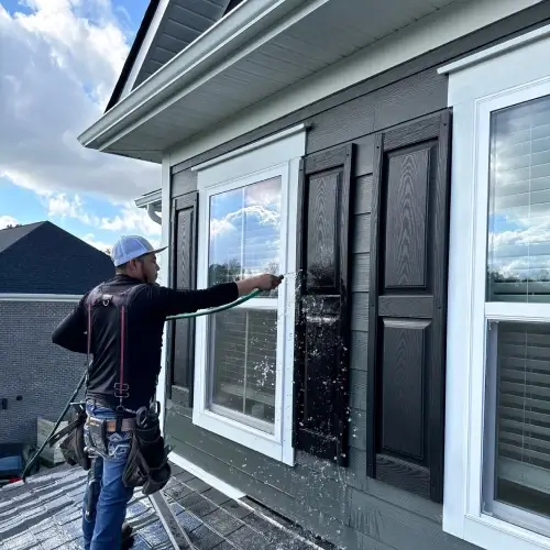 Choosing a siding contractor in Nixa, MO as Xtreme Exteriors technician cleans and inspects modern home siding and shutters