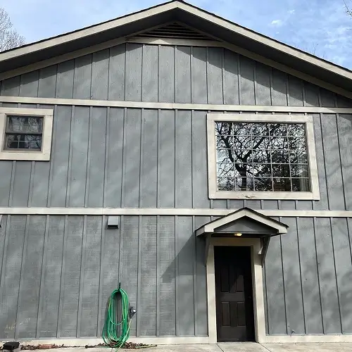 Contemporary gray board and batten siding with wide cream trim, large window, and black entry door on Nixa, MO home, featured in guide to siding by Xtreme Exteriors